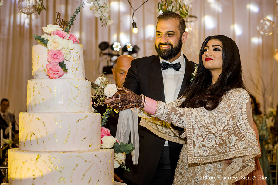 Bride wearing Ivory and white gown by Sabyasachi and groom wearing black tuxedo for reception