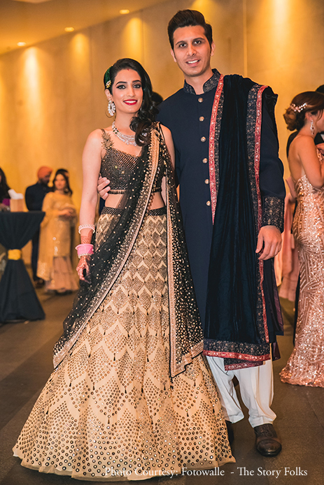 Bride in black and gold sequin lehenga by  Tarun Tahiliani and Groom in navy blue sherwani with a velvet shawl by Megaan