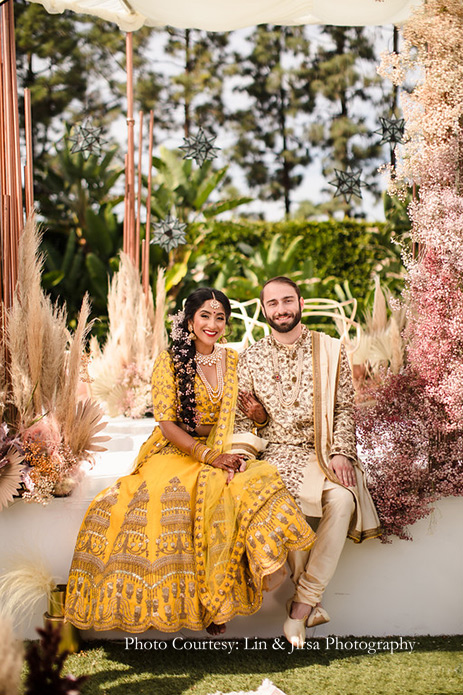 Bride wearing mustard yellow lehenga and customized kundan jewelry and Groom wearing beige sherwani for the wedding at USA