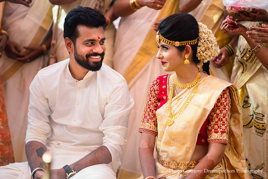 Bride in off-white and gold saree with a hand embroidered red blouse from Asmera and traditional jewelry