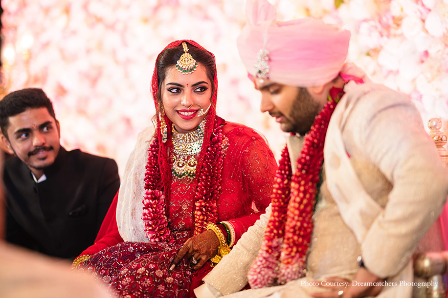 Bride wearing bright red anarkali with detailed embroidery and groom in and groom wearing ivory sherwani