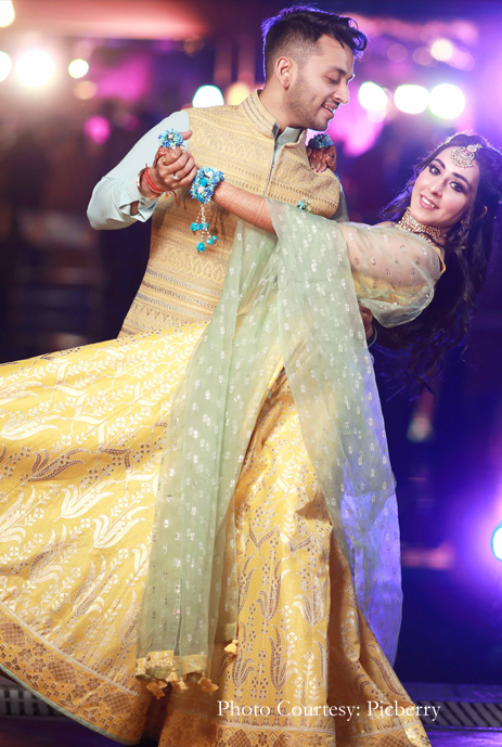 Bride in yellow and icy blue lehenga by Anita Dongre and groom in yellow and blue Bandi jacket kurta set by Shantanu and Nikhil