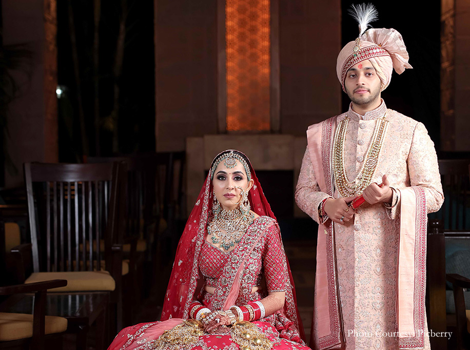 Bride wearing red lehenga and kundan jewelry and groom wearing peach sherwami