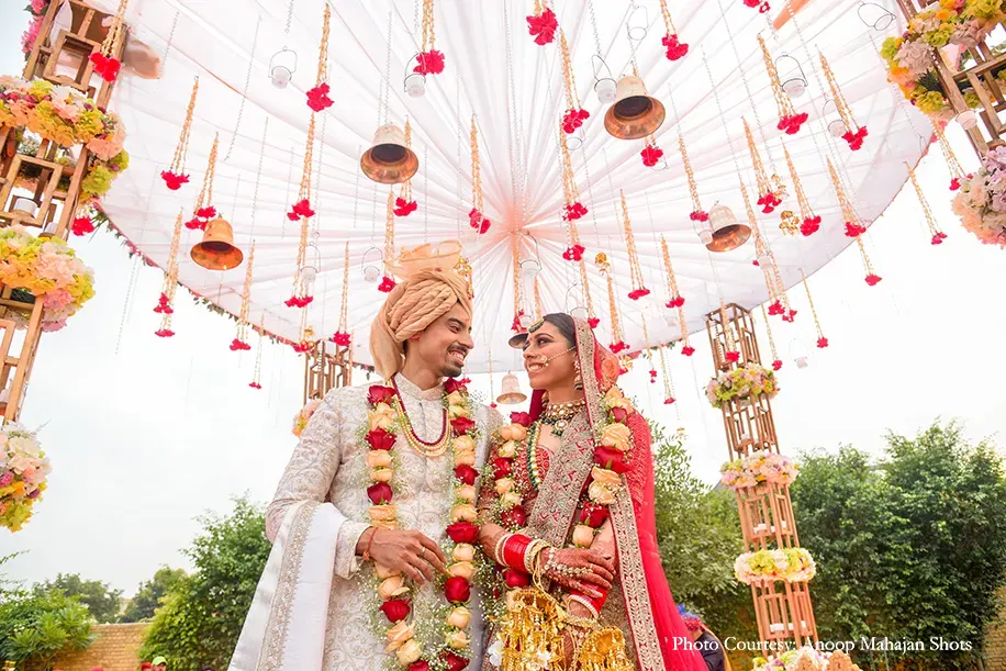 Bride wearing Red and gold lehenga and green kundan jewelry and groom wearing white sherwani for the wedding