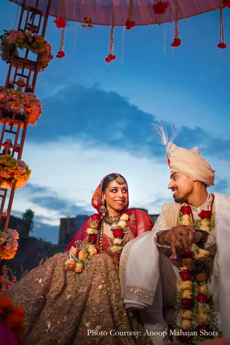 Bride wearing Red and gold lehenga and green kundan jewelry and groom wearing white sherwani for the wedding