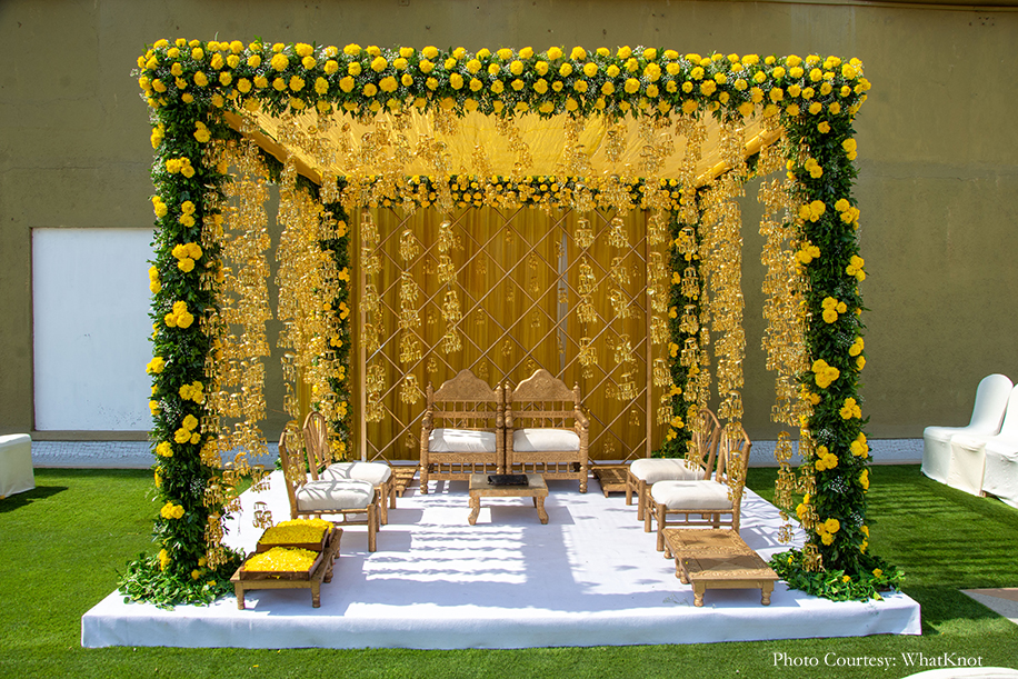 mandap decor with yellow drapes, lots of greens, fresh marigolds, and gold kalires dangling from the ceiling
