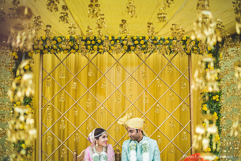 mandap decor with yellow drapes, lots of greens, fresh marigolds, and gold kalires dangling from the ceiling