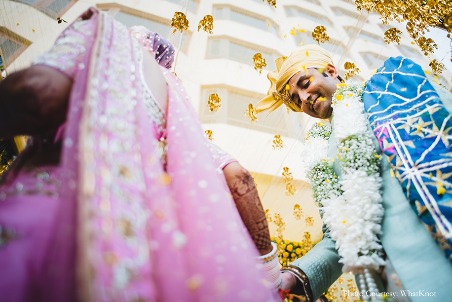 Bride wearing onion pink lehenga by Neeta Lulla with gold motifs, pearls, and sequins work, and the groom donned a soft pearl-blue sherwani
