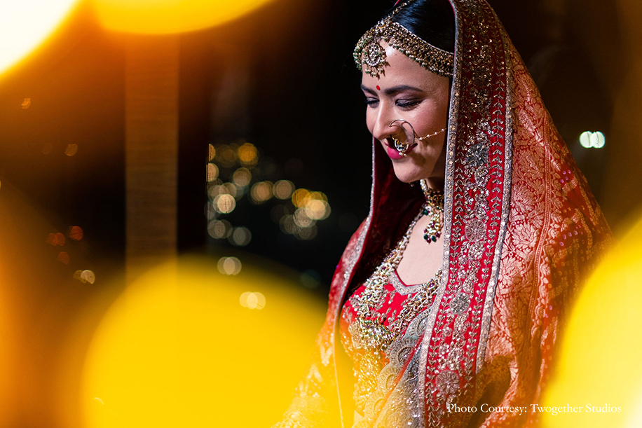 Bride wearing red and gold embroidered lehenga, statement nath and maang tikka for her wedding at The Leela Ambience, Gurugram
