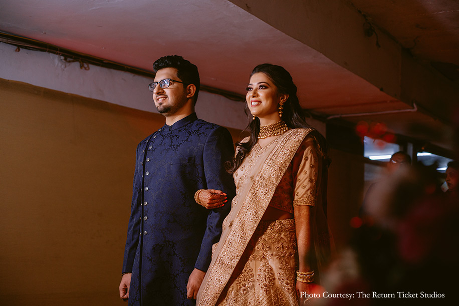 Bride wearing beige lehenga and groom in navy blue bandh gala
