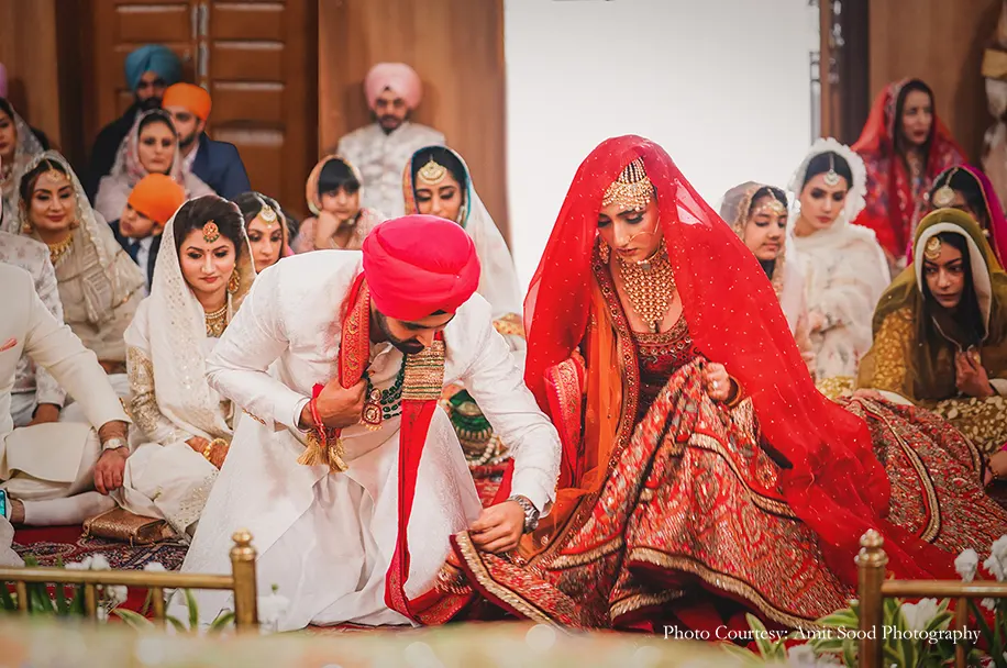 Groom wearing white sherwani with red safa and bride wearing red lehenga for the sikh wedding
