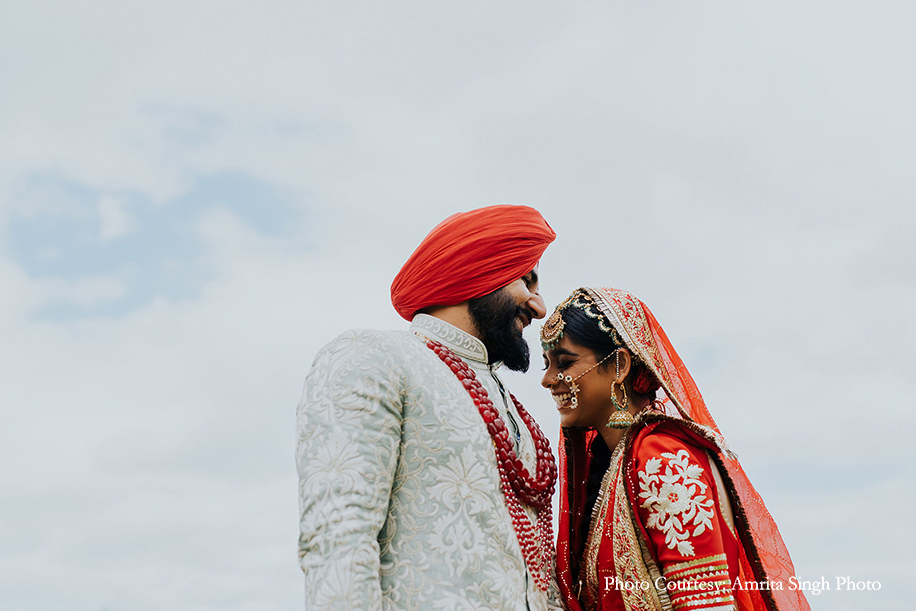 Red bridal lehenga with statement polki jewelry and traditional red and gold chooda and groom wearing off-white sherwani with red dupatta for anand karaj