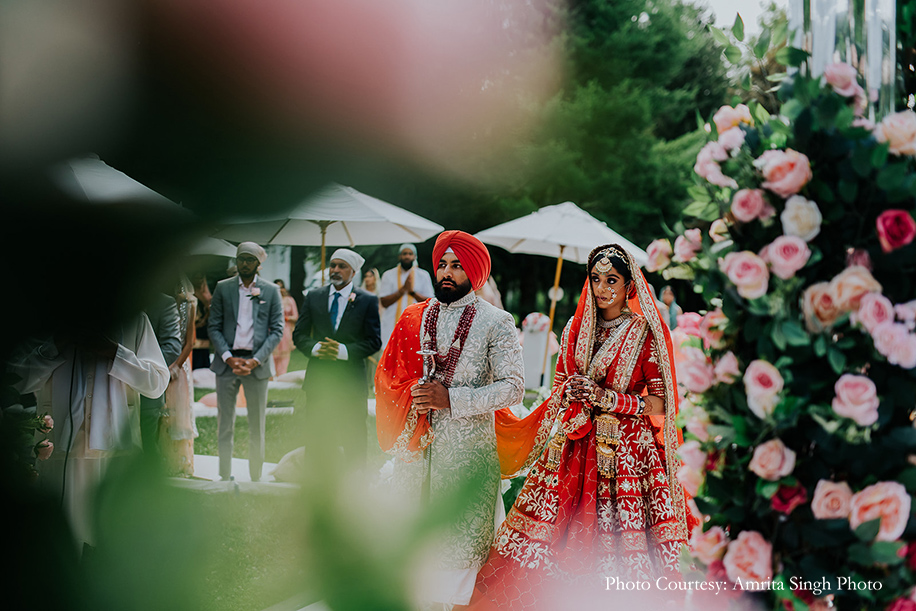 Red bridal lehenga with statement polki jewelry and traditional red and gold chooda and groom wearing off-white sherwani with red dupatta for anand karaj