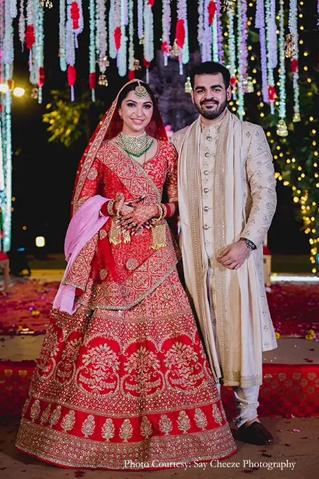 Bride in red lehenga and groom in beige gold embroidery sherwani by Sabyasachi