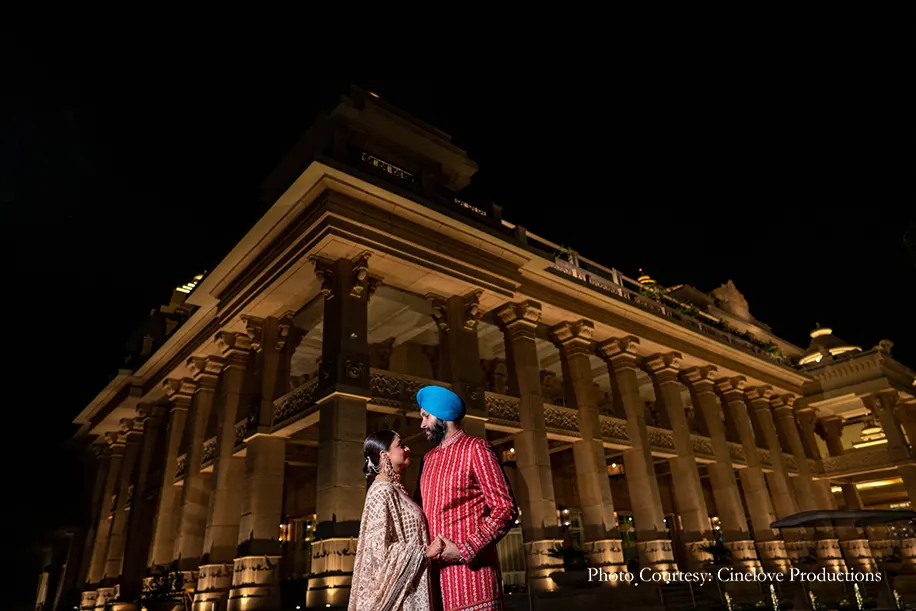 bride wearing Nawabi elegance in an off-shoulder embroidered cream lehenga and a Mughal passa and groom wearing red kurta with blue tarban for the dhol night at ITC Grand, Gurgaon