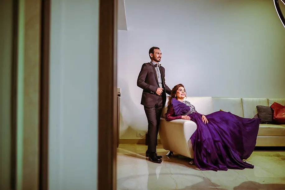Bride wearing purple gown and groom wearing black tuxedo for the sangeet