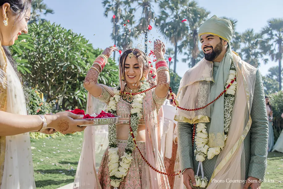 Bride wearing blush lehenga and groom wearing grey sherwani with jacket