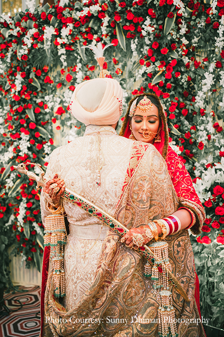Bride wearing Rajasthani embroidery red and turquoise lehenga and groom in Off-white sherwani with an elaborate Kalgi and Mala