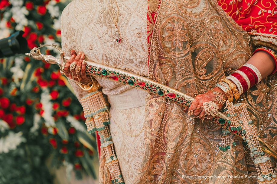 Bride wearing Rajasthani embroidery red and turquoise lehenga and groom in Off-white sherwani with an elaborate Kalgi and Mala