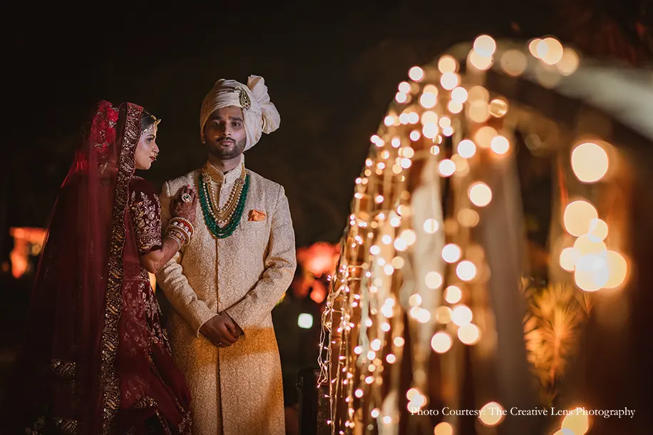 Bride wearing maroon lehenga and groom wearing off-white sherwani with safa