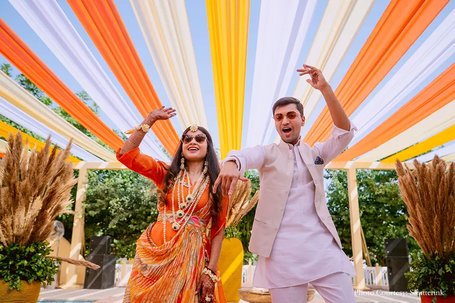 Bride on orange outfit and froom wearing off-white Nehru Jacket for the haldi