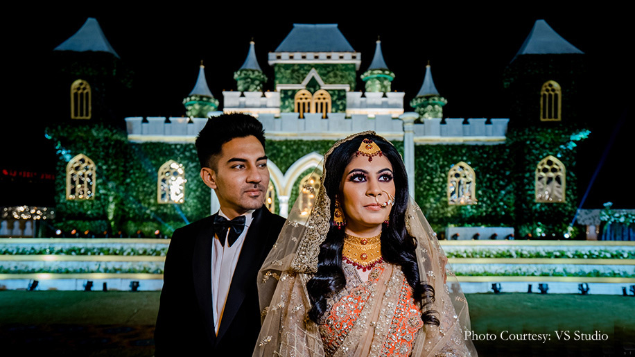 Bride wearing beige and orange outfit by Esha Sethi Thirani while groom wearing Black tuxedo by Sood for reception