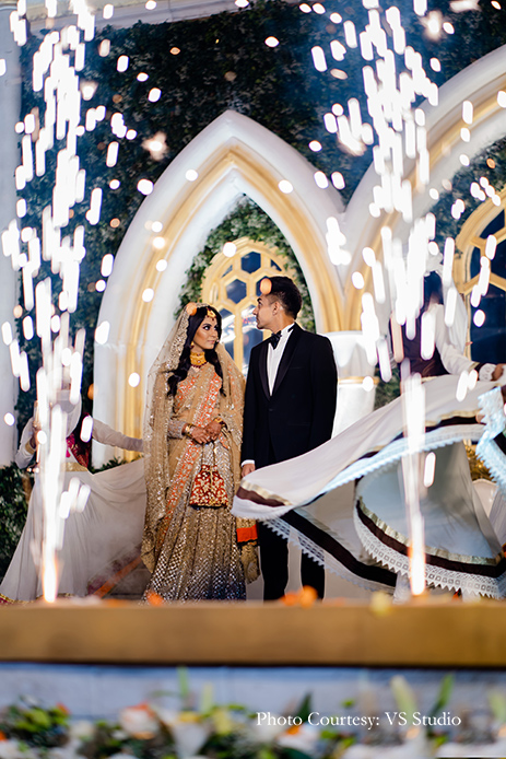 Bride wearing beige and orange outfit by Esha Sethi Thirani while groom wearing Black tuxedo by Sood for reception
