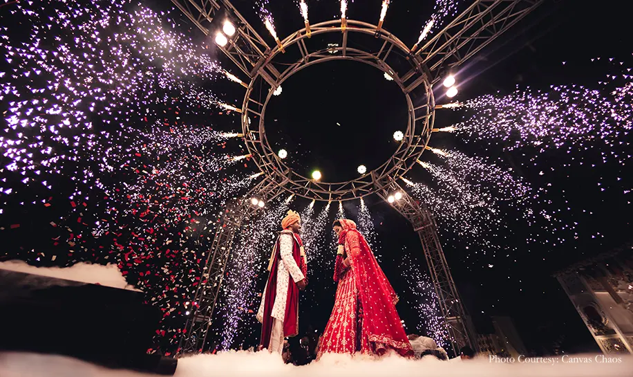 Bride wearing red lehenga and groom wearing off-white sherwani with the maroon shawl