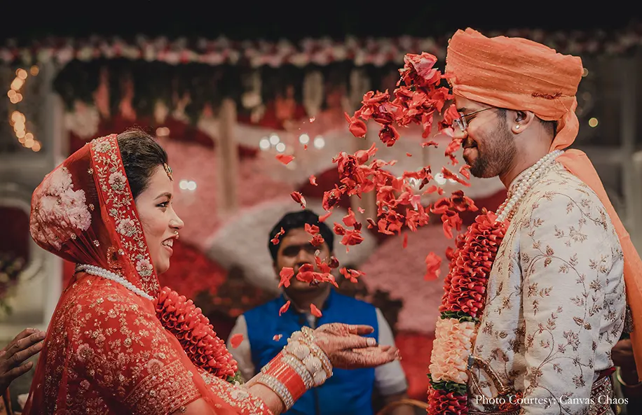 Bride wearing red lehenga and groom wearing off-white sherwani with the maroon shawl